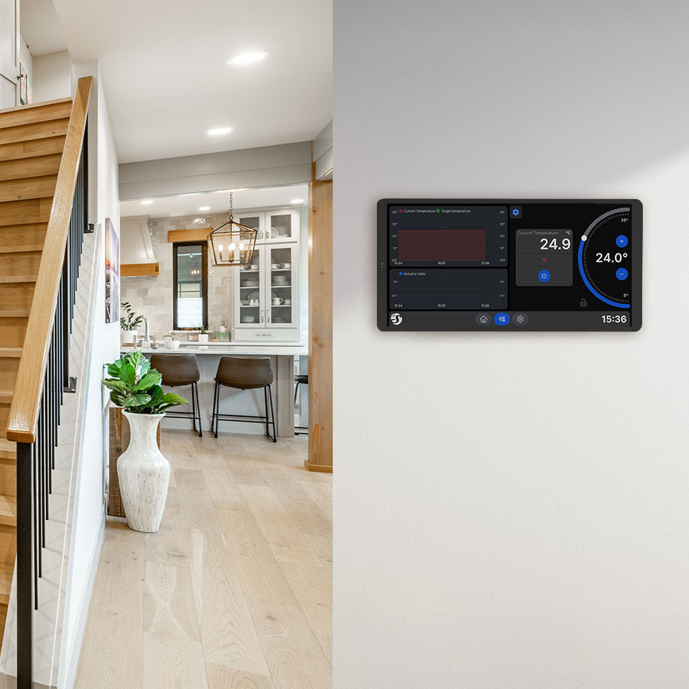 A modern home interior showcasing a wooden staircase and a Shelly Wall Display X2i Black smart thermostat mounted on a light-colored wall, with the kitchen and dining area visible in the background.